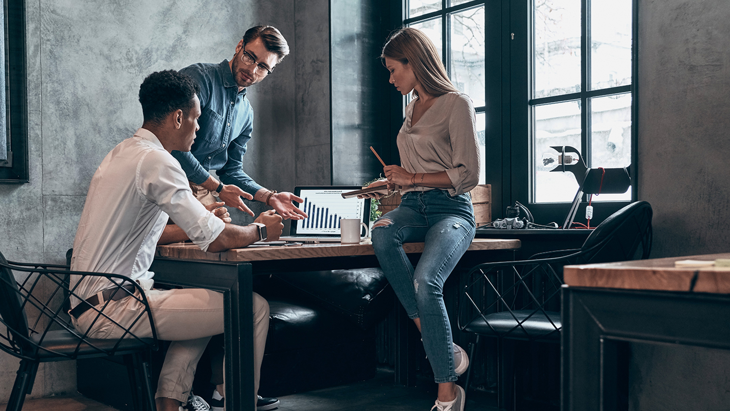 Three young people in smart casual wear analyzing data on laptop while working in office