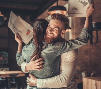 Two happy employees hug each other after seeing positive results in their charts.