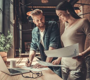 Two people working in a busy office environment, smiling and collaborating happily.
